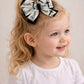 Child with a white shirt and two black and white hair bows with crosses on a plain background