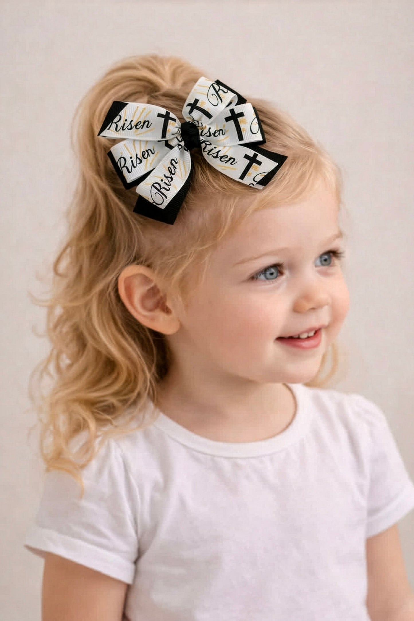 Child with a white shirt and two black and white hair bows with crosses on a plain background
