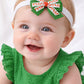Baby wearing a green dress and headband with a large decorative bow on a white background
