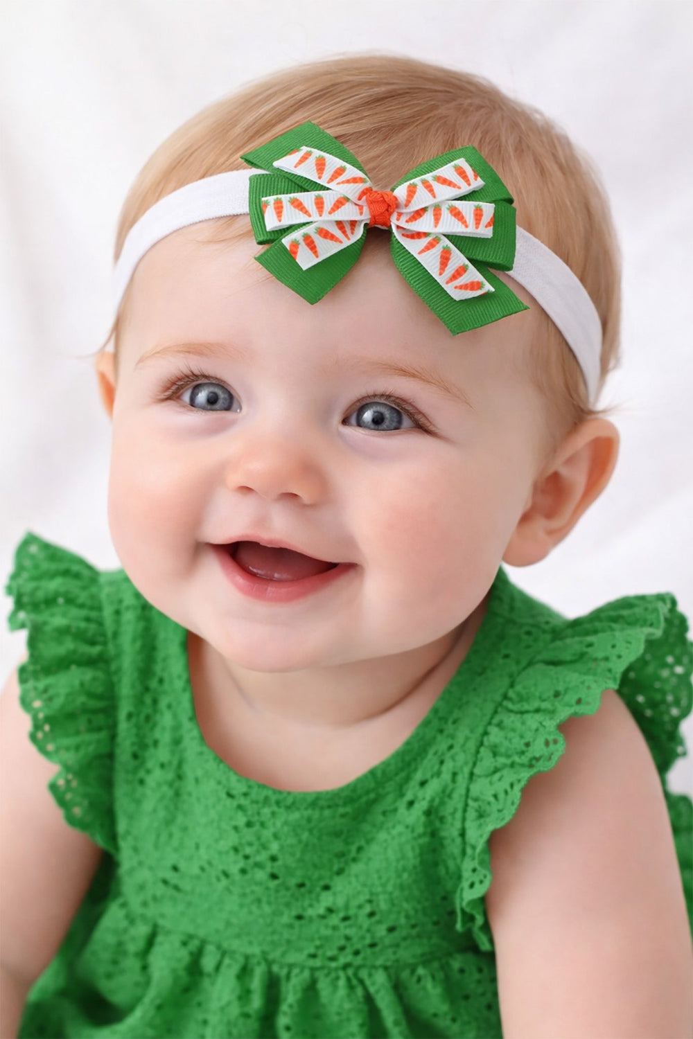 Baby wearing a green dress and headband with a large decorative bow on a white background