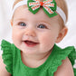 Baby wearing a green dress and headband with a large decorative bow on a white background